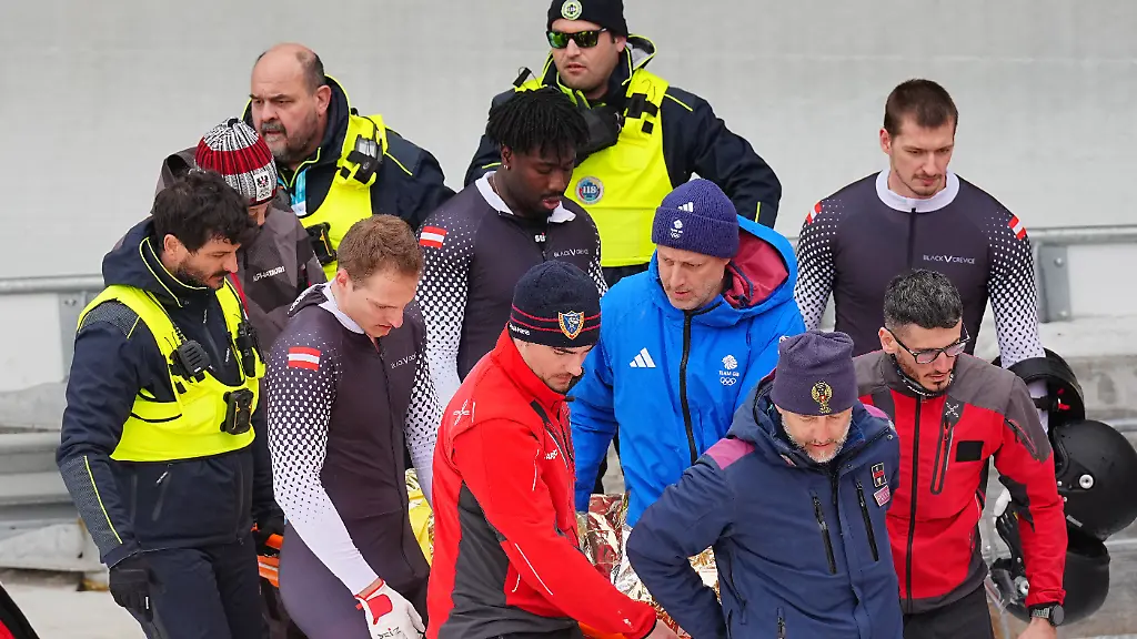 Olympia-Olympische-Winterspiele-Mailand-Cortina-2026-Bob-Viererbob-Maenner-Lauf-2-im-Cortina-Sliding-Centre-die-Besatzung-vom-Bob-aus-Oesterreich-Daniel-Bertschler-l-Sebastian-Mitterer-r-und-Daiyehan-Nichols-Bardi-M-sowie-medizinisches-Personal-und-Sicherheitspersonal-tragen-den-Piloten-Jakob-Mandlbauer-von-der-Unfallstelle