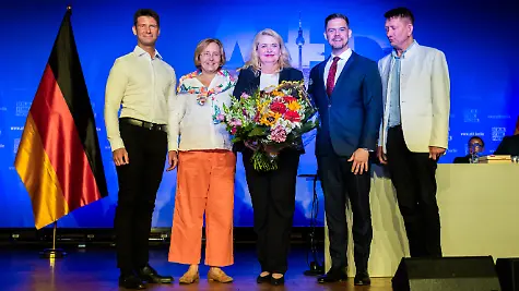 Kristin-Brinker-M-AfD-Spitzenkandidatin-fuer-die-Wahl-zum-Berliner-Abgeordnetenhaus-und-Landesvorsitzende-der-Berliner-AfD-steht-mit-Rene-Aust-AfD-l-Mitglied-des-Europaeischen-Parlaments-Beatrix-von-Storch-2-v-l-stellvertretenden-Fraktionsvorsitzenden-der-AfD-Bundestagsfraktion-Hannes-Gnauck-AfD-2-v-r-Mitglied-des-Deutschen-Bundestages-und-Ronald-Glaeser-r-stellvertretender-Landesvorsitzender-der-AfD-Berlin-nach-ihrer-symbolischen-Kuer-zur-Kandidatin-fuer-das-Amt-des-Regierenden-Buergermeisters-beim-Parteitag-der-AfD-Berlin-im-Stahlpalast-in-Brandenburg-an-der-Havel-mit-einem-Blumenstrauss-auf-der-Buehne-Auf-der-Tagesordnung-steht-unter-anderem-der-Beschluss-des-Wahlprogramms-zur-Wahl-des-Berliner-Abgeordnetenhauses-am-20-September-2026